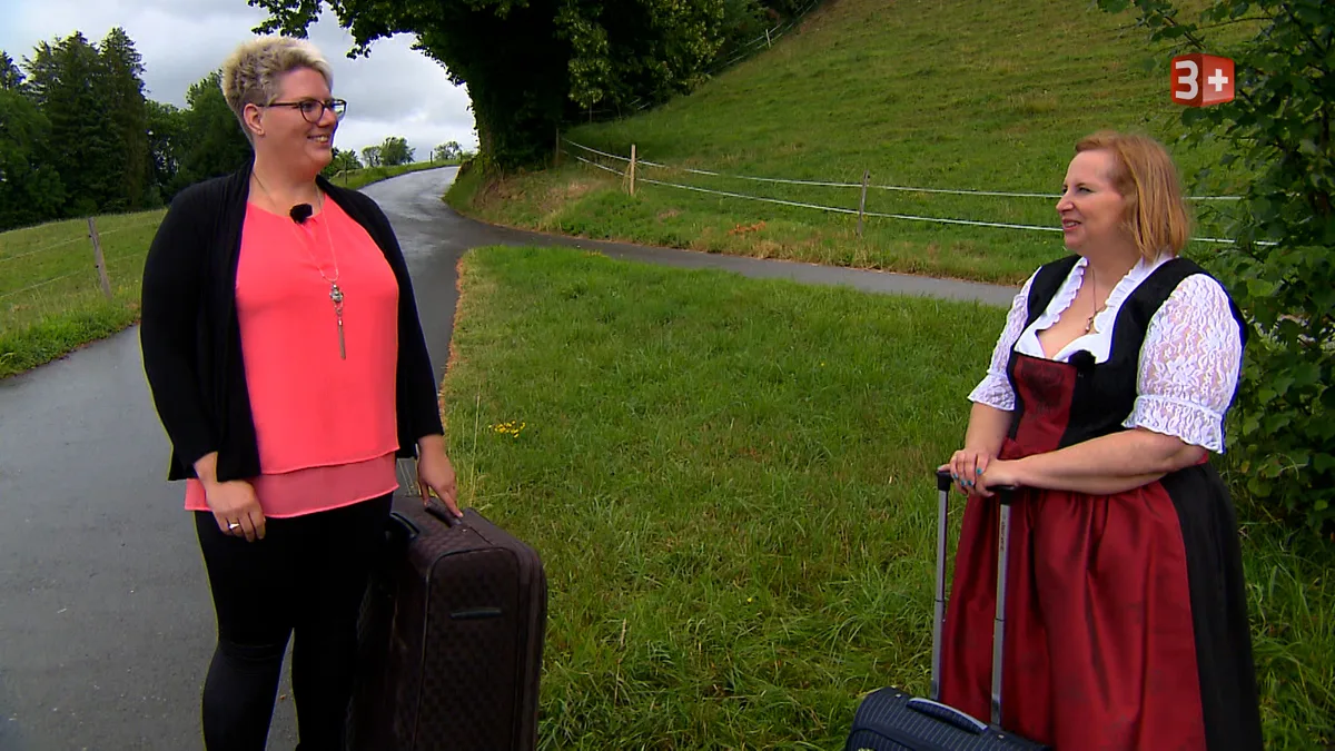 Man sieht eine Frau in leuchtend rosaroter Bluse und eine Frau im Dirndl.